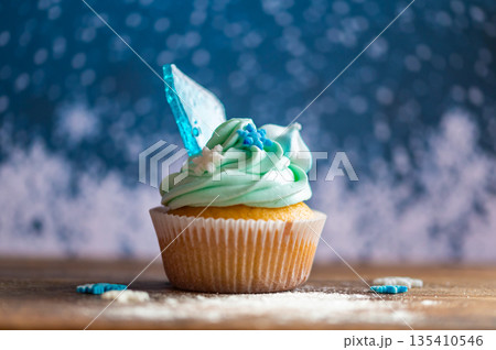 Homemade cupcake of blue color placed on wooden desk. Winter and christmas theme, snowflakes on cream with blue ice. Fresh and home baked sweet. Homemade cupcake of blue color placed on wooden desk. Winter and christmas theme, snowflakes on cream with blue ice. Fresh and home baked sweet. 135410546