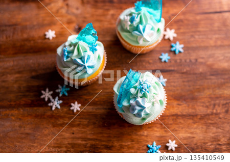 Homemade cupcake of blue color placed on wooden desk. Winter and christmas theme, snowflakes on cream with blue ice. Fresh and home baked sweet. Homemade cupcake of blue color placed on wooden desk. Winter and christmas theme, snowflakes on cream with blue ice. Fresh and home baked sweet. 135410549