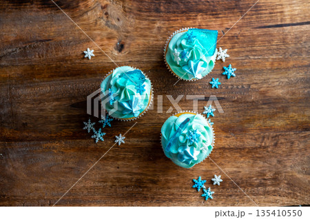 Homemade cupcake of blue color placed on wooden desk. Winter and christmas theme, snowflakes on cream with blue ice. Fresh and home baked sweet. Homemade cupcake of blue color placed on wooden desk. Winter and christmas theme, snowflakes on cream with blue ice. Fresh and home baked sweet. 135410550