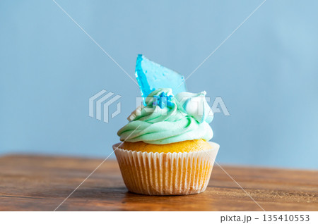 Homemade cupcake of blue color placed on wooden desk. Winter and christmas theme, snowflakes on cream with blue ice. Fresh and home baked sweet. Homemade cupcake of blue color placed on wooden desk. Winter and christmas theme, snowflakes on cream with blue ice. Fresh and home baked sweet. 135410553
