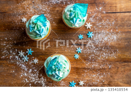 Homemade cupcake of blue color placed on wooden desk. Winter and christmas theme, snowflakes on cream with blue ice. Fresh and home baked sweet. 135410554