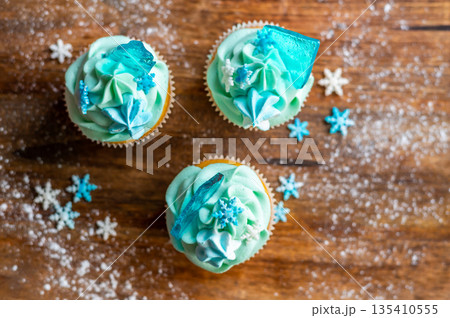 Homemade cupcake of blue color placed on wooden desk. Winter and christmas theme, snowflakes on cream with blue ice. Fresh and home baked sweet. 135410555