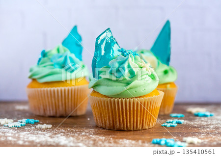 Homemade cupcake of blue color placed on wooden desk. Winter and christmas theme, snowflakes on cream with blue ice. Fresh and home baked sweet. 135410561