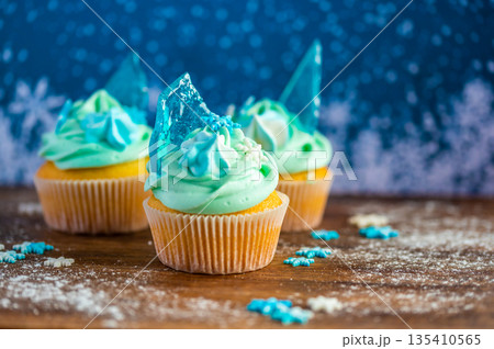 Homemade cupcake of blue color placed on wooden desk. Winter and christmas theme, snowflakes on cream with blue ice. Fresh and home baked sweet. Homemade cupcake of blue color placed on wooden desk. Winter and christmas theme, snowflakes on cream with blue ice. Fresh and home baked sweet. 135410565