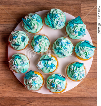 Homemade cupcake of blue color placed on wooden desk. Winter and christmas theme, snowflakes on cream with blue ice. Fresh and home baked sweet. Homemade cupcake of blue color placed on wooden desk. Winter and christmas theme, snowflakes on cream with blue ice. Fresh and home baked sweet. 135410575