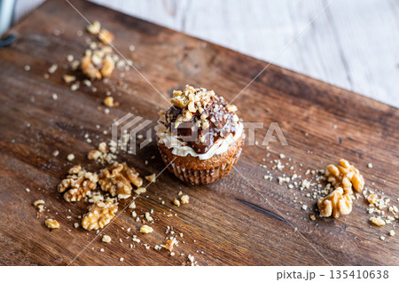 Tasty chocolate muffin with creme mascarpone and chocolate on top, covered with nuts. Placed on wooden desk. Sweet fresh and homemade cupcake. Tasty chocolate muffin with creme mascarpone and chocolate on top, covered with nuts. Placed on wooden desk. Sweet fresh and homemade cupcake. 135410638