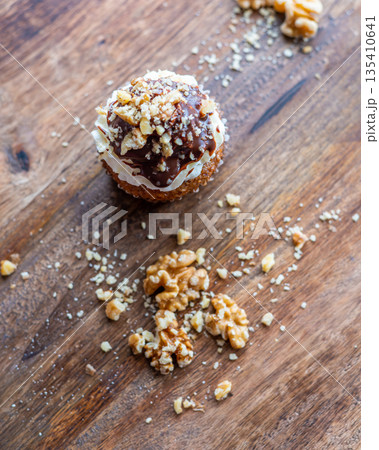 Tasty chocolate muffin with creme mascarpone and chocolate on top, covered with nuts. Placed on wooden desk. Sweet fresh and homemade cupcake. Tasty chocolate muffin with creme mascarpone and chocolate on top, covered with nuts. Placed on wooden desk. Sweet fresh and homemade cupcake. 135410641