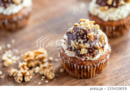 Tasty chocolate muffin with creme mascarpone and chocolate on top, covered with nuts. Placed on wooden desk. Sweet fresh and homemade cupcake. Tasty chocolate muffin with creme mascarpone and chocolate on top, covered with nuts. Placed on wooden desk. Sweet fresh and homemade cupcake. 135410659