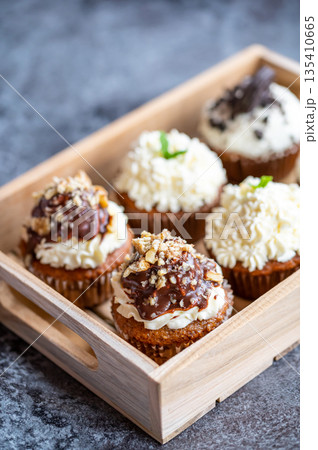 Cupcakes and muffins placed in wooden box. Chocolate and creme with nuts. Fresh home make baked sweets. Cupcakes and muffins placed in wooden box. Chocolate and creme with nuts. Fresh home make baked sweets. 135410665