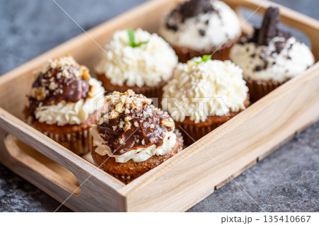 Cupcakes and muffins placed in wooden box. Chocolate and creme with nuts. Fresh home make baked sweets. 135410667