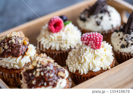 Tasty sweet muffins with mascarpone creme and chocolate, raspberry and blueberry. Fresh home baked sweets with fruit. Placed in wooden box. Tasty sweet muffins with mascarpone creme and chocolate, raspberry and blueberry. Fresh home baked sweets with fruit. Placed in wooden box. 135410678