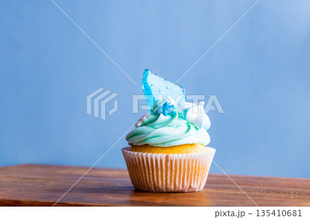 Homemade cupcake of blue color placed on wooden desk. Winter and christmas theme, snowflakes on cream with blue ice. Fresh and home baked sweet. 135410681