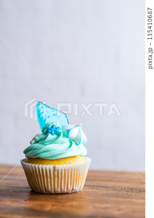 Homemade cupcake of blue color placed on wooden desk. Winter and christmas theme, snowflakes on cream with blue ice. Fresh and home baked sweet. Homemade cupcake of blue color placed on wooden desk. Winter and christmas theme, snowflakes on cream with blue ice. Fresh and home baked sweet. 135410687