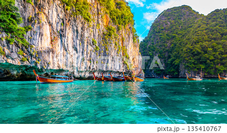 View of long tail boats on turquoise water at ocean near Ko Phi Phi islands, Thailand. Concept of exotic vacation in tropical paradise. Limestone rock in background. 135410767