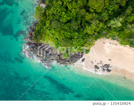 Aerial top down view of tropical beach with turquoise water, white sand and big rock. Trees and palms growing on the rock. Tropical theme. 135410924