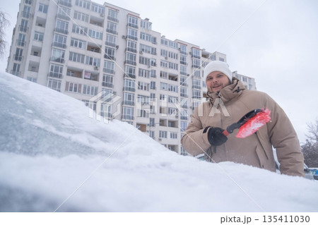 Man Clearing Snow from Car in Winter Cityscape Man Clearing Snow from Car in Winter Cityscape 135411030