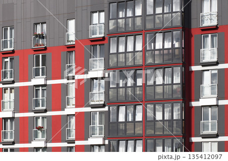 Close-up of modern residential building facade with red and gray panels and large glass balconies. Close-up of modern residential building facade with red and gray panels and large glass balconies. 135412097