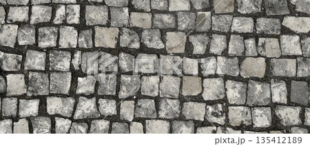 Stone pavement cobblestone surface with gray and beige square blocks, rough texture and weathered 135412189