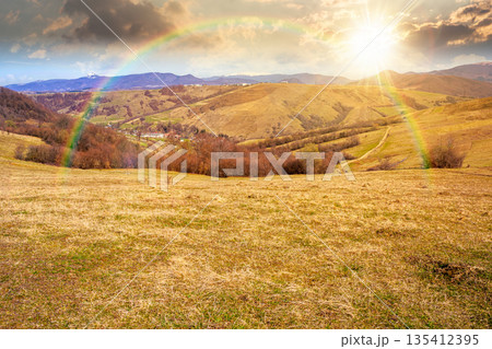 rural landscape with village in valley at sunset. outdoor adventures in countryside with rolling hills and snowy mountains in early spring in evening light. storytelling cinematic image under rainbow rural landscape with village in valley at sunset. outdoor adventures in countryside with rolling hills and snowy mountains in early spring in evening light. storytelling cinematic image under rainbow 135412395