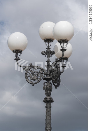 Vintage street lamp with decorative design against cloudy sky. Urban detail, classic city atmosphere and minimal composition 135415069