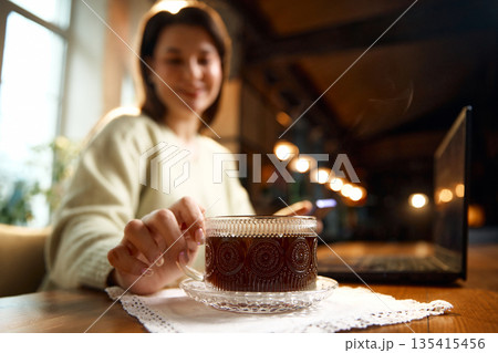 Coffee cup on saucer with woman hand reaching across wooden table. 135415456