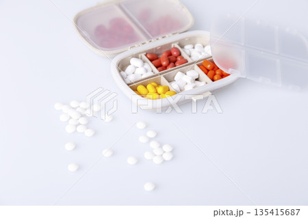 Pill box with colorful pills and vitamins. Plastic beige container with cells for medicines. Health concept. Selective focus, close-up. Pill box with colorful pills and vitamins. Plastic beige container with cells for medicines. Health concept. Selective focus, close-up. 135415687