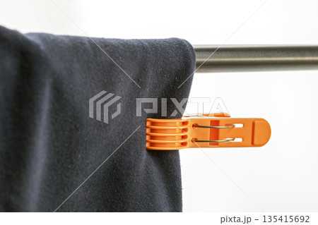 A close-up view of an orange plastic clothespin securing dark blue fabric to a shiny metal rod, part of a clothes drying rack. 135415692