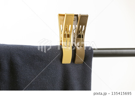Two plastic clothespins, two beige and one brown, firmly secure a dark blue fabric onto a metal rod isolated on white background Two plastic clothespins, two beige and one brown, firmly secure a dark blue fabric onto a metal rod isolated on white background 135415695