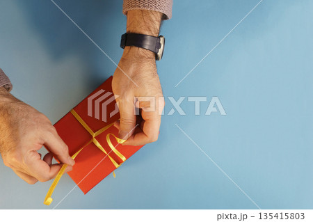 Man hands untying yellow ribbon on red gift box with large copy space. 135415803