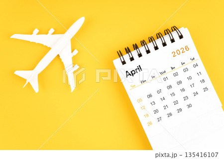 April 2026 calendar and airplane toy on yellow background. 135416107