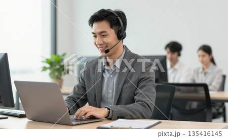 Asian IT support staff wearing headset assisting clients via laptop in a modern professional office 135416145