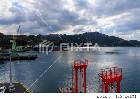 愛媛県八幡浜港の全景パノラマ 貨物船と緑クレーン 紅葉山を配した曇り空の港湾貿易風景 135416181