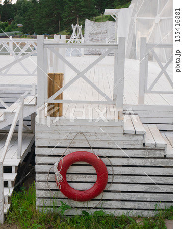Red lifebuoy hanging on white wooden pier or beach platform with railing. Safety equipment for water rescue or emergency for summer vacation. Red lifebuoy hanging on white wooden pier or beach platform with railing. Safety equipment for water rescue or emergency for summer vacation. 135416881