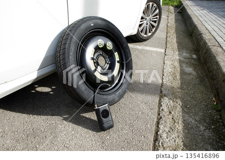 a temporary spare wheel resting on the car, ready to be changed 135416896