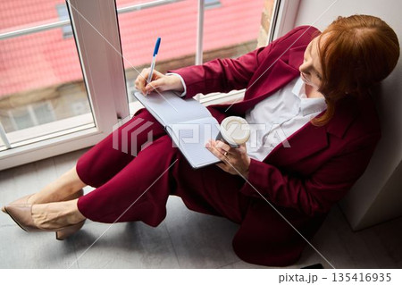 Woman concentrating on presentation while enjoying coffee by window Woman concentrating on presentation while enjoying coffee by window 135416935