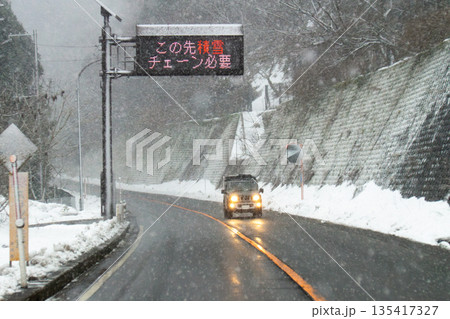 雪が降り注ぐ峠道とチェーン装着の電光掲示板 雪が降り注ぐ峠道とチェーン装着の電光掲示板 135417327