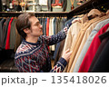 Handsome man consumer choosing clothing in vintage second hand boutique, picking jacket from hanger. 135418026