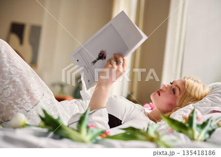 Woman enjoying peaceful magazine reading, Female lying comfortably on plush bedding among blooming tulips 135418186