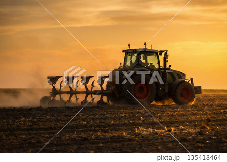 Tractor plowing field at sunset. Agricultural machinery working in soil. 135418464