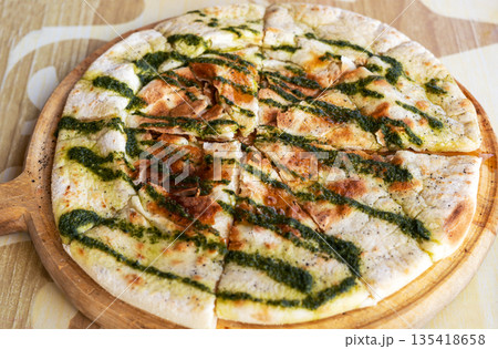 Freshly baked focaccia flatbread sliced on wooden board and drizzled with green pesto sauce. Traditional Italian bread with crispy crust, served on a rustic table. Mediterranean cuisine and bakery Freshly baked focaccia flatbread sliced on wooden board and drizzled with green pesto sauce. Traditional Italian bread with crispy crust, served on a rustic table. Mediterranean cuisine and bakery 135418658