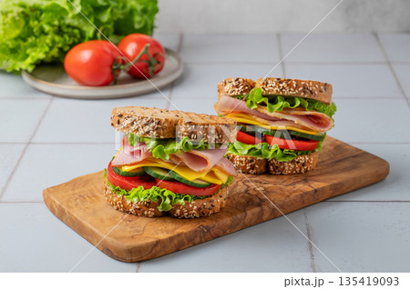 Two sandwich or toasts with ham, cheese, lettuce and vegetables on a wooden board Two sandwich or toasts with ham, cheese, lettuce and vegetables on a wooden board 135419093