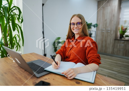 Focused woman writes notes while working at a stylish home office 135419951