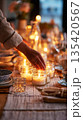 A person is placing simple candles inside jars on a dining table. The setup takes place in a casual home kitchen during the evening and creates a cozy atmosphere 135420567