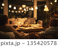 People sit in a small living room after finishing their meal. Friends enjoy talking and relaxing while drinks are on the table and soft lights glow in the background 135420578
