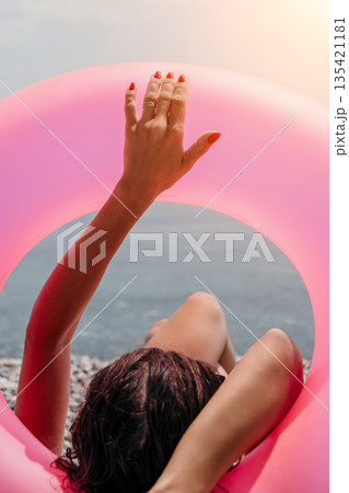 Swim ring relaxation beach woman resting on a pebble shore holding a pink inflatable circle during a bright sunny summer vacation at the seaside Swim ring relaxation beach woman resting on a pebble shore holding a pink inflatable circle during a bright sunny summer vacation at the seaside 135421181