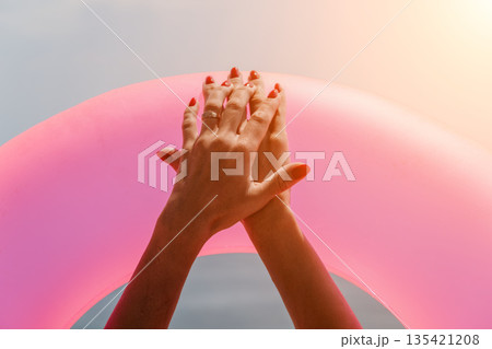 Woman hands pool floating on pink inflatable ring during summer vacation by the water under bright sun 135421208