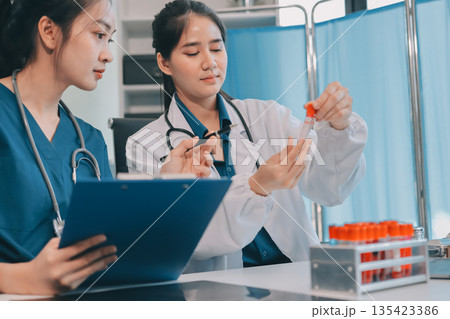 Medical team meeting analyzing blood test results in hospital laboratory. Doctors and scientists in lab coats are having a discussion about blood test result, holding test tubes and taking notes. Medical team meeting analyzing blood test results in hospital laboratory. Doctors and scientists in lab coats are having a discussion about blood test result, holding test tubes and taking notes. 135423386