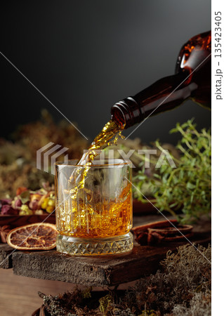 Herbal bitter liqueur is poured from a vintage bottle into a glass. Herbal bitter liqueur is poured from a vintage bottle into a glass. 135423405