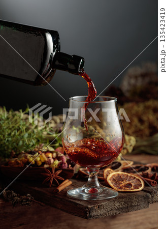 Herbal bitter liqueur is poured from a vintage bottle into a glass. Herbal bitter liqueur is poured from a vintage bottle into a glass. 135423419