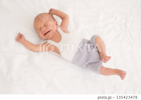 A crying, screaming newborn wakes up lying on the bed. Restless sleep with children's colic in the tummy. Infant health and care A crying, screaming newborn wakes up lying on the bed. Restless sleep with children's colic in the tummy. Infant health and care 135423478